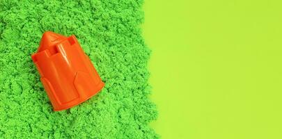 vert cinétique le sable avec Orange Plastique le sable moule dans forme de Château la tour. des gamins sensoriel jeu, la modélisation de coloré sable. lumière vert papier Contexte avec copie espace, longue bannière. photo