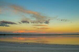 une le coucher du soleil plus de une Lac avec des nuages réfléchi dans le l'eau photo