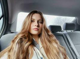 Jeune femme avec longue cheveux, ondulé coiffure dans le voiture ou Taxi taxi comme passager, explorant le ville, transport et Voyage photo