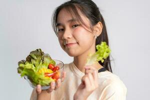 portrait de une content espiègle asiatique fille en mangeant Frais salade de une verre bol après faire des exercices à maison. Jeune Dame profiter en bonne santé nutrition et biologique nourriture, ayant végétarien repas photo