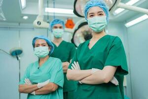 portrait de asiatique femmes chirurgien et infirmière avec médical masque permanent avec bras franchi dans opération théâtre à une hôpital. équipe de professionnel chirurgiens. soins de santé, urgence médical un service concept photo