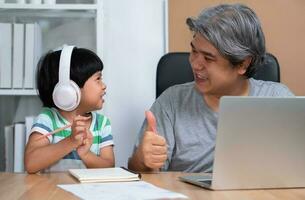 asiatique père est travail à le Accueil avec une fille et en train d'étudier en ligne apprentissage de école ensemble. Nouveau mode de vie Ordinaire pendant une quarantaine. concept de rester maison, free-lance et paternité concept photo