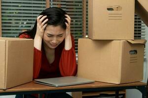 triste asiatique femme emballage affaires dans une papier carton boîte et pleurs sur le bureau dans le Bureau après étant Licencier et sans emploi. concept de impact sur le économique ralentissement et la gestion de le échec photo