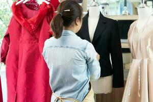 content Jeune asiatique femme couturière mode designer est vérification pour achèvement pour une costume et robe dans une salle d'exposition. concept de Succès Jeune entrepreneur dans le mode entreprise. photo