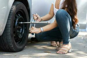 une femme asiatique intelligente et séduisante monte sa voiture et utilise une clé pour changer la roue d'une voiture cassée, utilise des outils ou de l'équipement, essaie de résoudre les problèmes par elle-même, la réparation automobile et le concept d'assurance photo