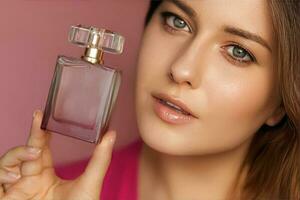 parfum, beauté produit et produits de beauté modèle visage portrait sur rose arrière-plan, magnifique femme en portant fragrance bouteille avec floral féminin flairer, mode et maquillage photo