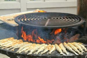 grillé poisson sur une en forme de bol plat gril avec Feu trou dans le centre. Extérieur Fruit de mer barbecue cuisson. pique-nique sur arrière-cour sur ouvert air. rue nourriture concept. en train de préparer poisson plus de ouvert feu de camp photo