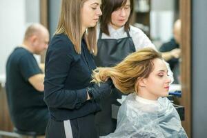 deux femelle les coiffeurs préparer longue cheveux de une Jeune femme fabrication boucles coiffure dans une beauté salon. photo