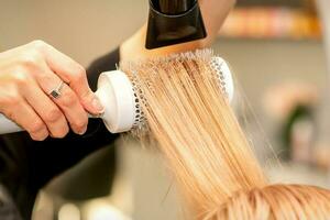 professionnel coiffeur sec cheveux avec une sèche-cheveux et rond brosse à cheveux dans une beauté salon. photo