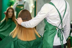 une femelle coiffeur est ratissage le longue marron cheveux de une Jeune femme à une parloir. photo