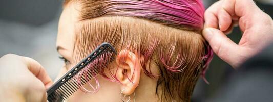 ratissage le cheveux de une Jeune femme pendant coloration cheveux dans rose Couleur à une cheveux salon proche en haut. photo