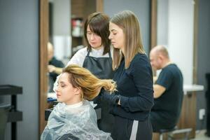 deux femelle les coiffeurs préparer longue cheveux de une Jeune femme fabrication boucles coiffure dans une beauté salon. photo