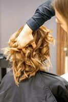 femelle coiffeur chèques marron frisé coiffure de une Jeune caucasien femme dans beauté salon. photo