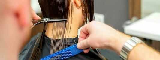 le Masculin coiffeur coupes retour femelle du client cheveux avec les ciseaux et peigne dans une beauté salon. photo