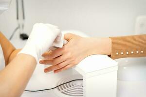 mains de une manucure dans blanc protecteur gants essuyer femelle ongles avec une papier serviette de table dans le salon. photo