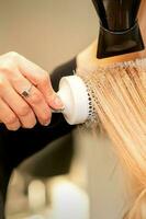 professionnel coiffeur sec cheveux avec une sèche-cheveux et rond brosse à cheveux dans une beauté salon. photo