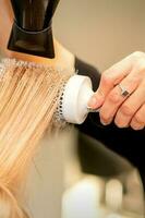 professionnel coiffeur sec cheveux avec une sèche-cheveux et rond brosse à cheveux dans une beauté salon. photo