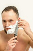 Jeune caucasien homme rasage barbe avec une gros couteau sur blanc Contexte. photo
