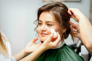 maquillage artiste appliquant crème rougir fondation tube sur le joue de le Jeune caucasien femme dans une beauté salon. photo