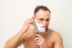 Jeune caucasien homme rasage barbe avec une gros couteau sur blanc Contexte. photo