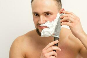Jeune caucasien homme rasage barbe avec une gros couteau sur blanc Contexte. photo