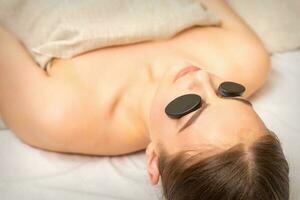 massage avec des pierres sur le yeux de Jeune femme avoir une traitement dans une beauté spa. photo
