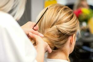 fermer coiffeur coiffant blond cheveux sur le retour de le tête dans une beauté salon. photo