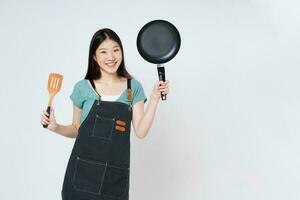 Jeune femme portant cuisine tablier cuisine et en portant la poêle et spatule isolé sur blanc Contexte. photo