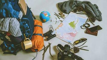 vacances de planification touristique à l'aide de la carte du monde avec d'autres accessoires de voyage autour. smartphone, appareil photo argentique et lunettes de soleil sur fond blanc. sac à dos de voyage