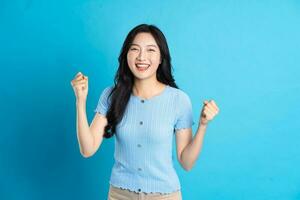 portrait de une content souriant asiatique fille posant sur une bleu Contexte photo