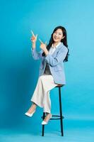 asiatique femme d'affaires portrait séance sur chaise, isolé sur bleu Contexte photo