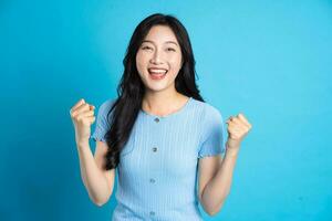 portrait de une content souriant asiatique fille posant sur une bleu Contexte photo