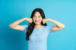 portrait de une content souriant asiatique fille posant sur une bleu Contexte photo