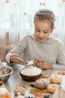 mignonne peu fille met farine dans une verre pour cuisine gingembre pâte pour fabrication biscuits pour Halloween dans le Accueil cuisine. traite et les préparatifs pour le Halloween fête photo