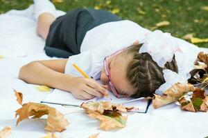 fatigué de l'écriture devoirs, une écolière allonger vers le bas à se détendre sur une couverture dans un l'automne ensoleillé parc. Extérieur éducation. retour à école concept photo