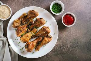 épicé cuit poulet pilons avec vert oignons et sésame des graines sur une assiette Haut vue photo