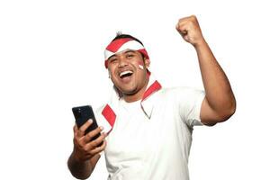 excité asiatique homme portant blanc T-shirt souriant tandis que en portant le sien téléphone, isolé par blanc Contexte. indonésien indépendance journée fête photo