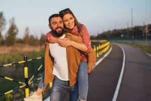 content souriant couple profiter le coucher du soleil. homme est porter sur retour le sien femme. photo