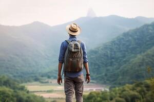 retour vue de Jeune homme avec sac à dos et chapeau permanent sur Haut de le Montagne photo