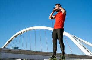 Jeune homme en train de préparer à courir avec une paire de écouteurs dans de face de une pont photo