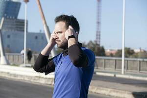 une fermer coup de une Jeune Masculin écoute à la musique avec écouteurs tandis que le jogging dans le rue photo