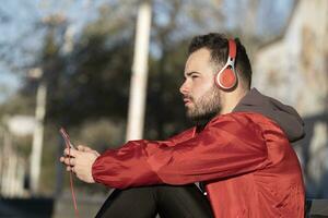 une fermer coup de une Jeune Masculin dans rouge casque de musique écoute à la musique tandis que travail en dehors dans le rue photo