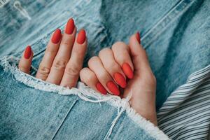 magnifique femelle mains avec une brillant rouge mat manucure sur une Contexte de jean. élégant ovale clou conception. été manucure. copie espace. photo