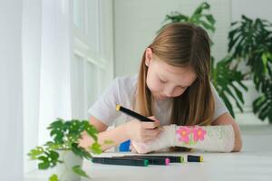 une peu fille des peintures une jeter sur sa bras. une enfant dessine une dessin sur une jeter après une main blessure. photo