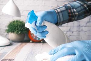 main dans des gants en caoutchouc bleu tenant une table de nettoyage de flacon pulvérisateur