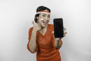 une de bonne humeur asiatique femme portant rouge kebaya et Bandeau, montrant sa téléphone tandis que faire des gestes D'accord signe avec sa des doigts, isolé par blanc Contexte. l'indonésie indépendance journée concept photo