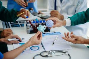 médical équipe ayant une réunion avec médecins dans blanc laboratoire manteaux et chirurgical gommages assise à une table discuter une les patients travail en ligne en utilisant des ordinateurs dans le médical industrie photo