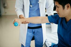 asiatique physiothérapeute portion Masculin patient élongation bras pendant exercice correct avec haltère dans main pendant formation main dans hôpital photo