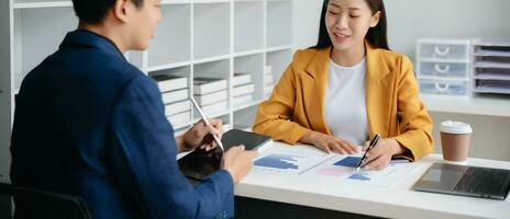 un collègue d'affaires asiatique présente et explique et utilise un ordinateur portable et une tablette. travail d'équipe, équipe de marketing financier, assis dans un bureau moderne. photo