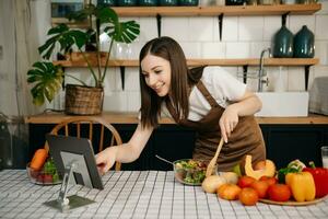 Jeune femme cuisine dîner a vidéo appel conversation dans cuisine. souriant content femelle parlant avec ami en utilisant application sur ordinateur. photo